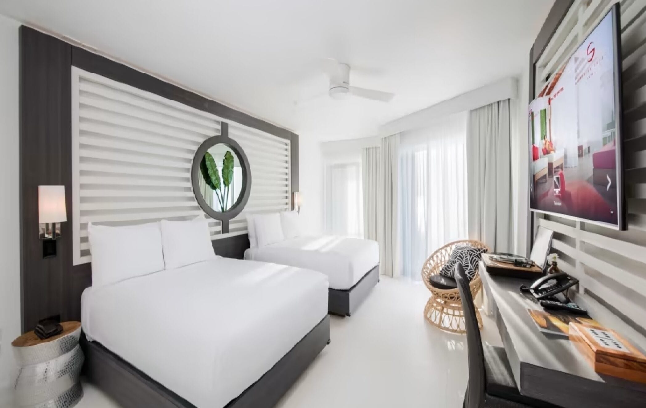 A hotel room with two beds, a TV, a desk with a phone, and a wall-mounted mirror.