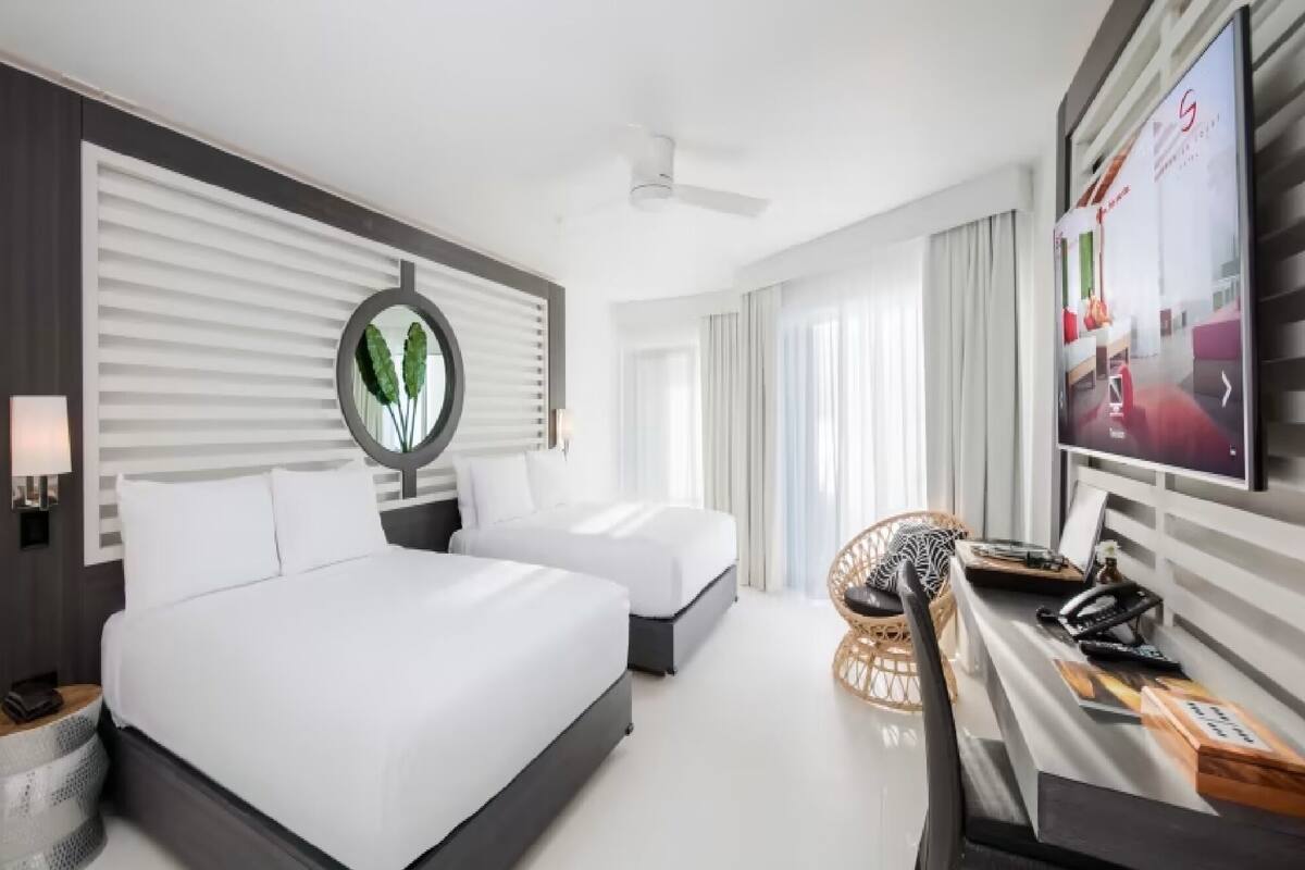 A hotel room with two beds, a TV, a desk with a phone, and a wall-mounted mirror.