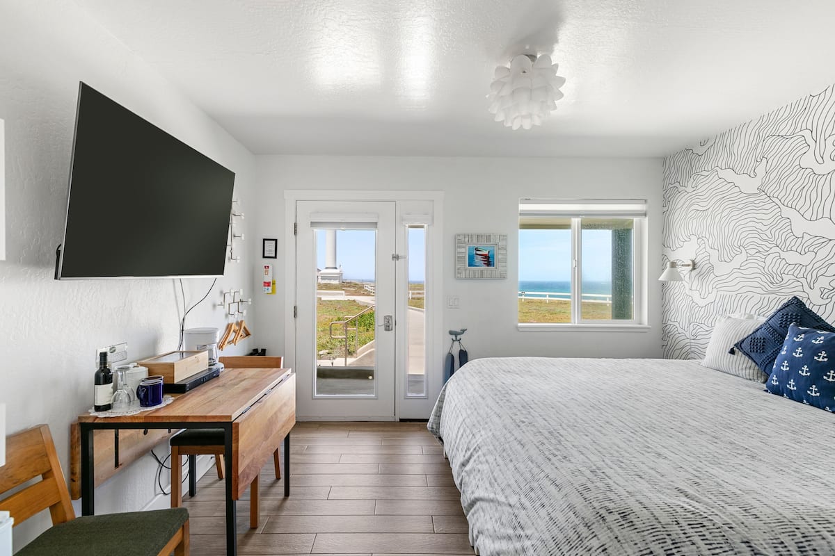Quarto com cama, escrivaninha, cadeira, televisão e janela com vista.