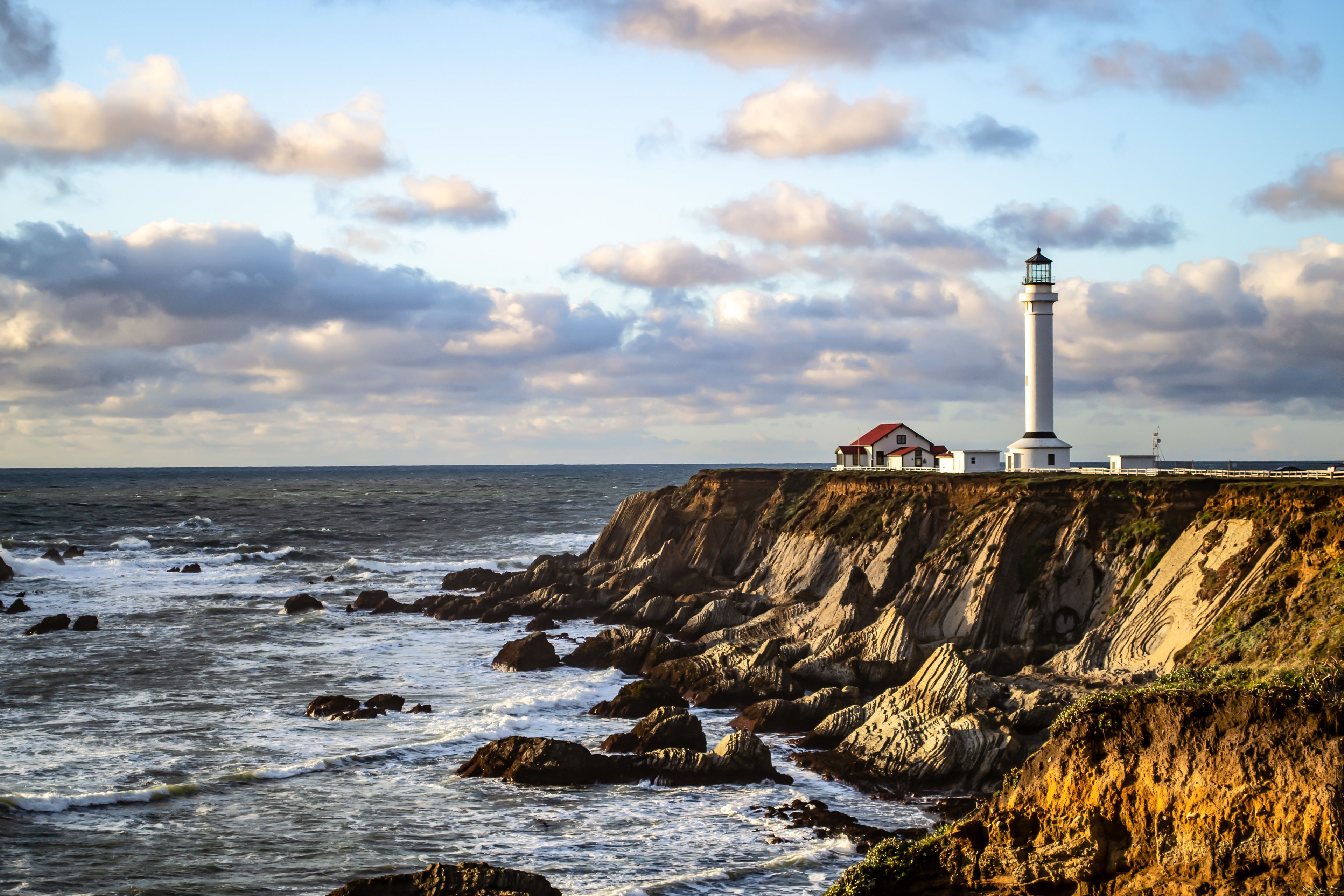 Un faro en una costa rocosa con un edificio cercano.