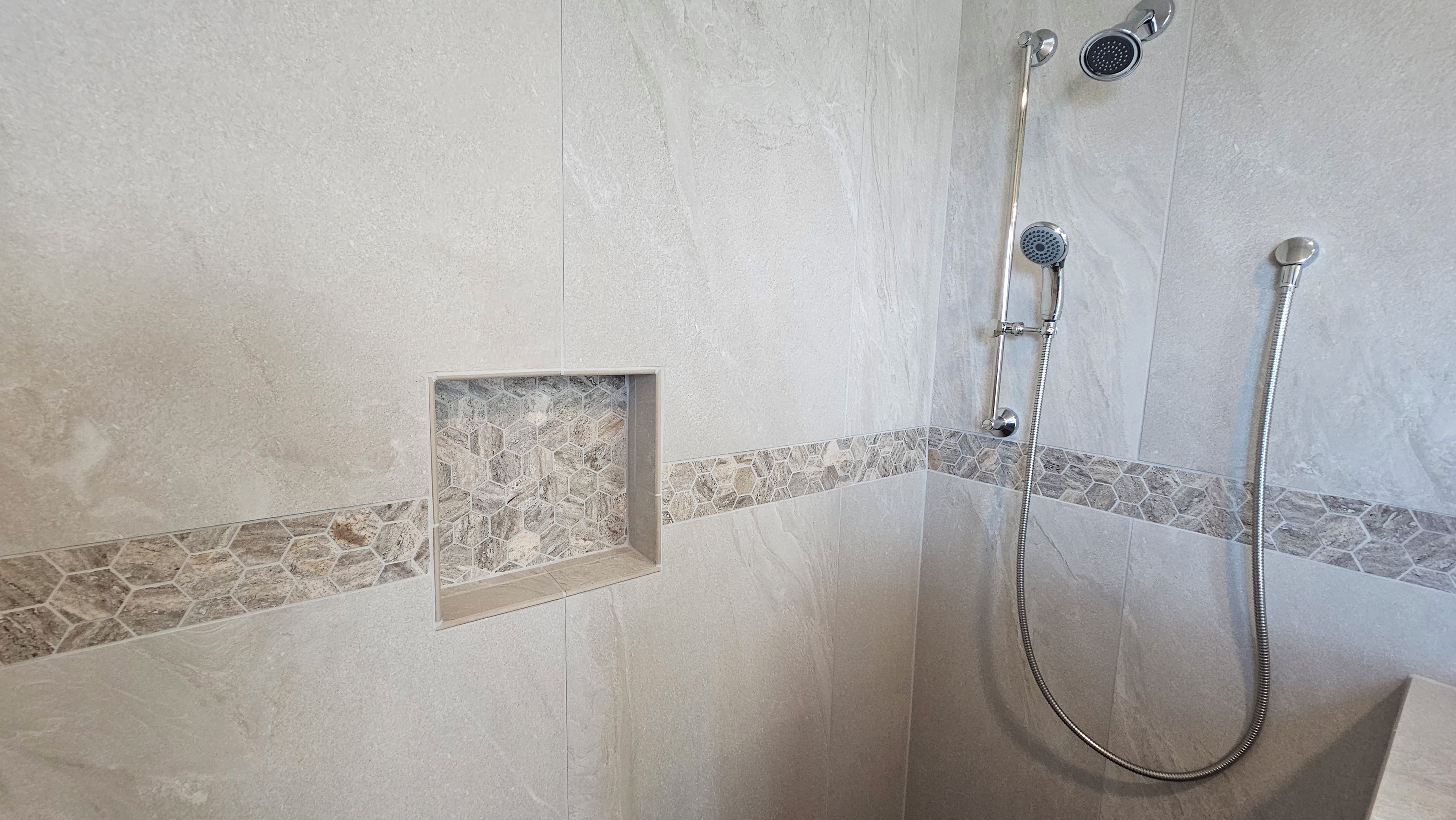 A shower area with a tiled wall, a hexagonal tile accent, and a handheld showerhead.