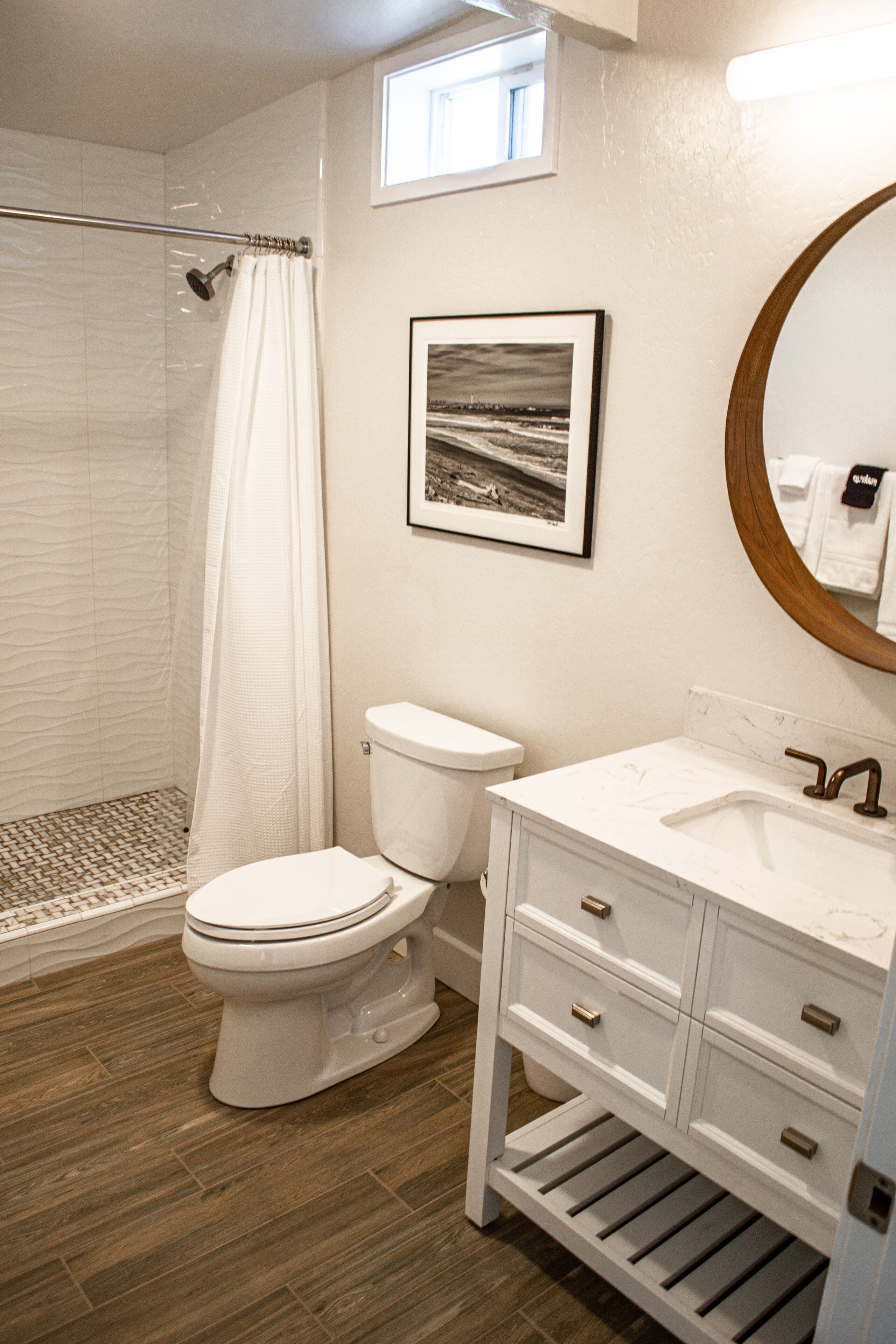 A bathroom with a shower, toilet, sink, and a framed picture on the wall.
