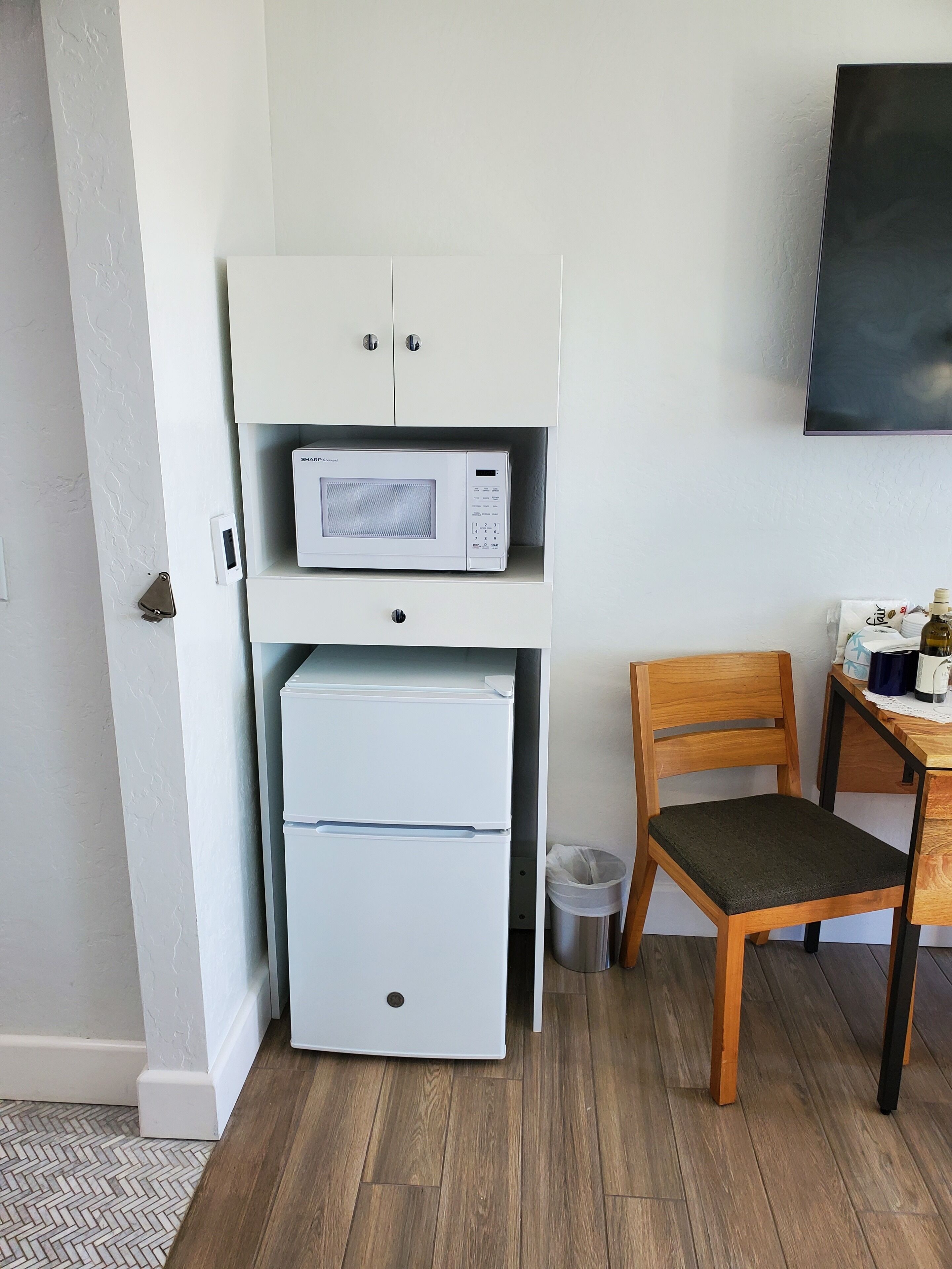 A compact kitchenette with a microwave, refrigerator, and wooden chair.