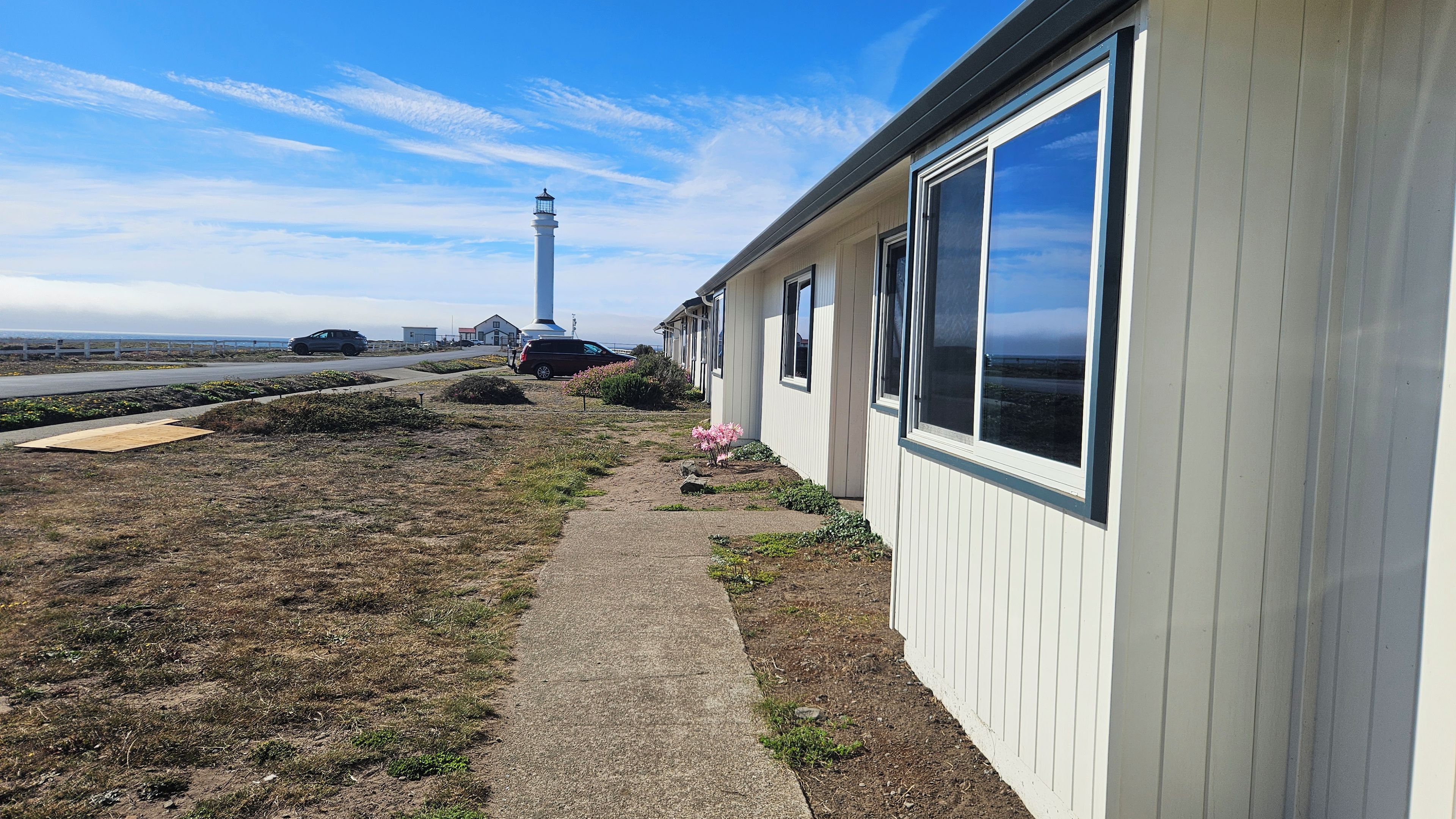 A coastal property with a lighthouse in the background, a paved walkway, and a row of windows on the building.