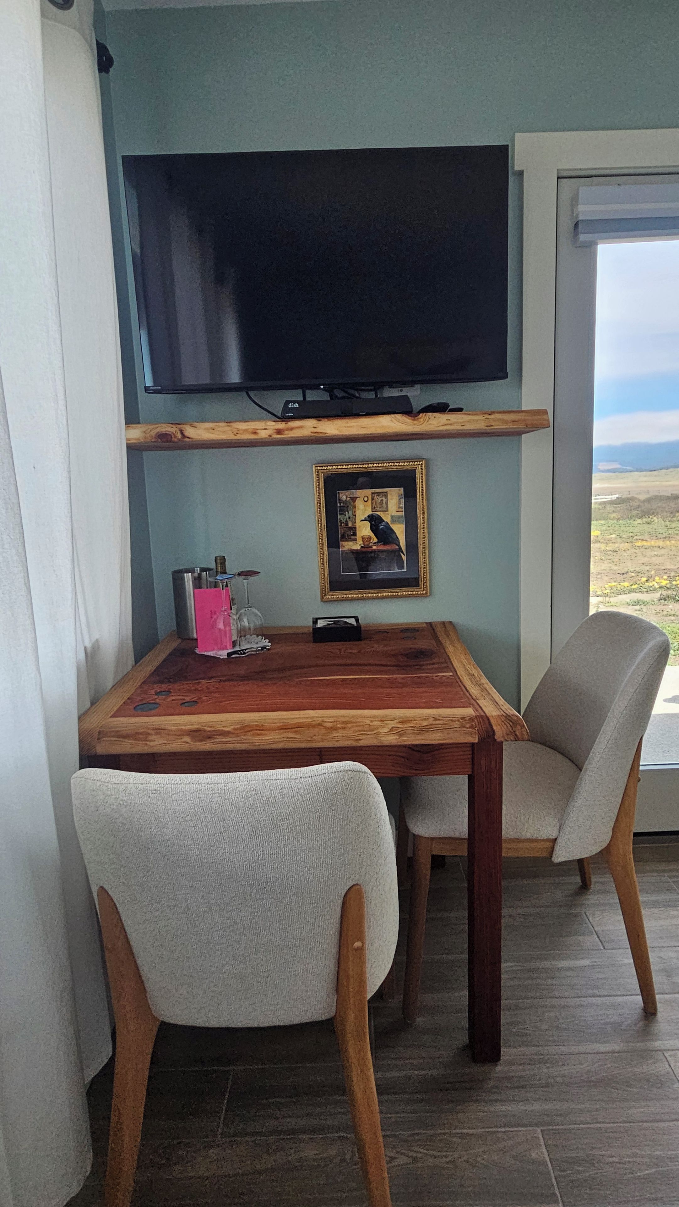 A dining area with a table, chairs, a flat-screen TV mounted on the wall, and a framed picture on the wall.