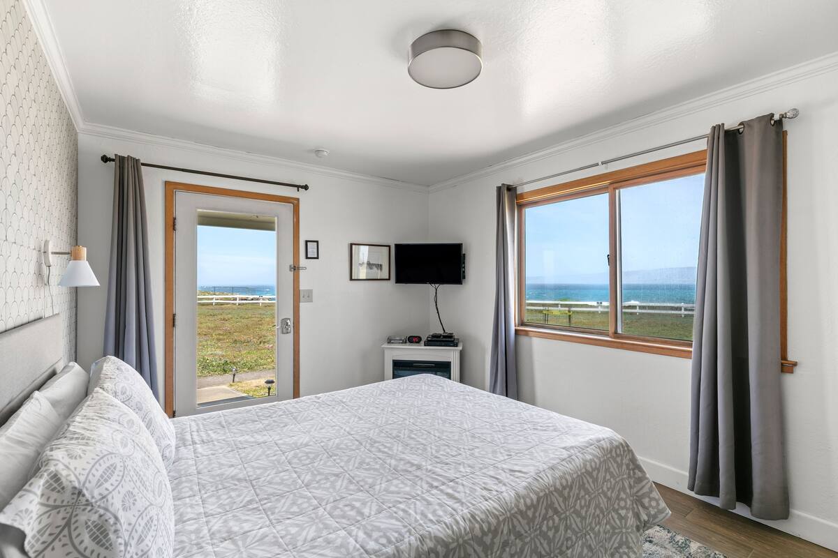 Quarto com cama, televisão, uma mesinha com aquecedor e vista para o mar pela janela.