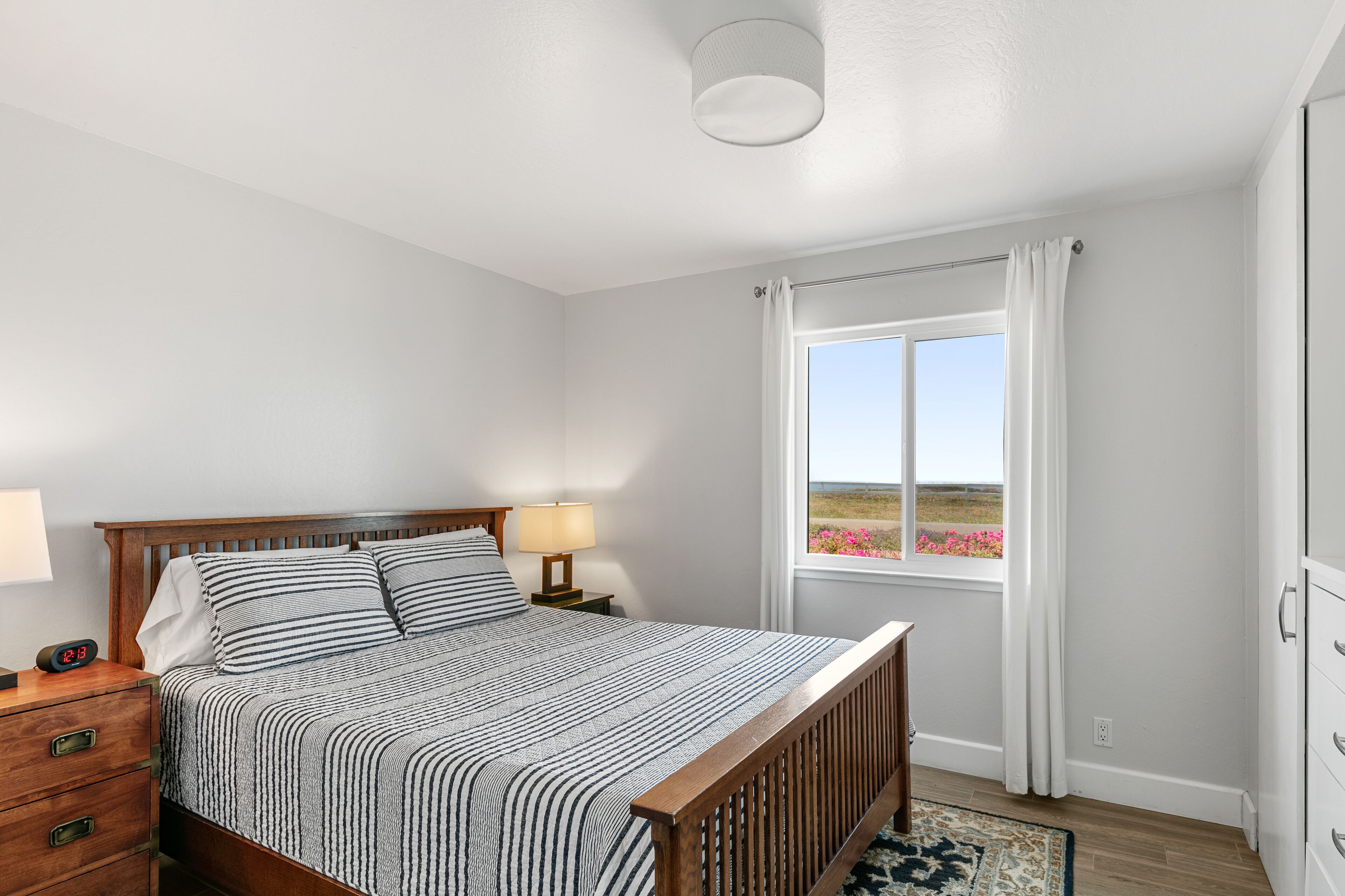Un dormitorio con cama, mesita de noche, lámpara y una ventana con cortinas.