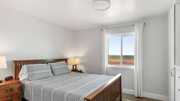 Un dormitorio con cama, mesita de noche, lámpara y una ventana con cortinas.