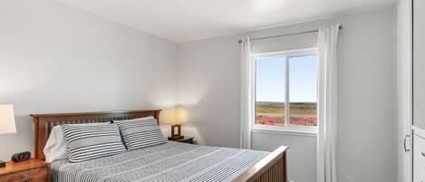 Un dormitorio con cama, mesita de noche, lámpara y una ventana con cortinas.