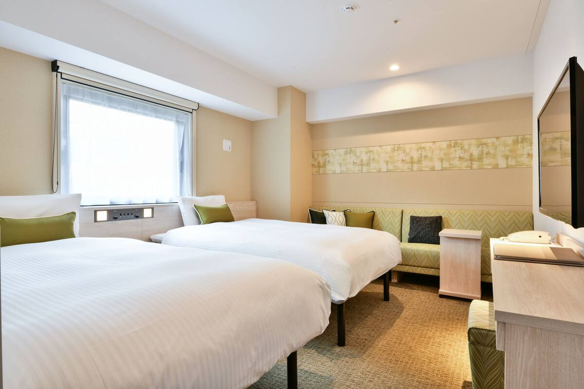 A hotel room with two beds, a desk, a chair, a nightstand, and a large window with curtains.