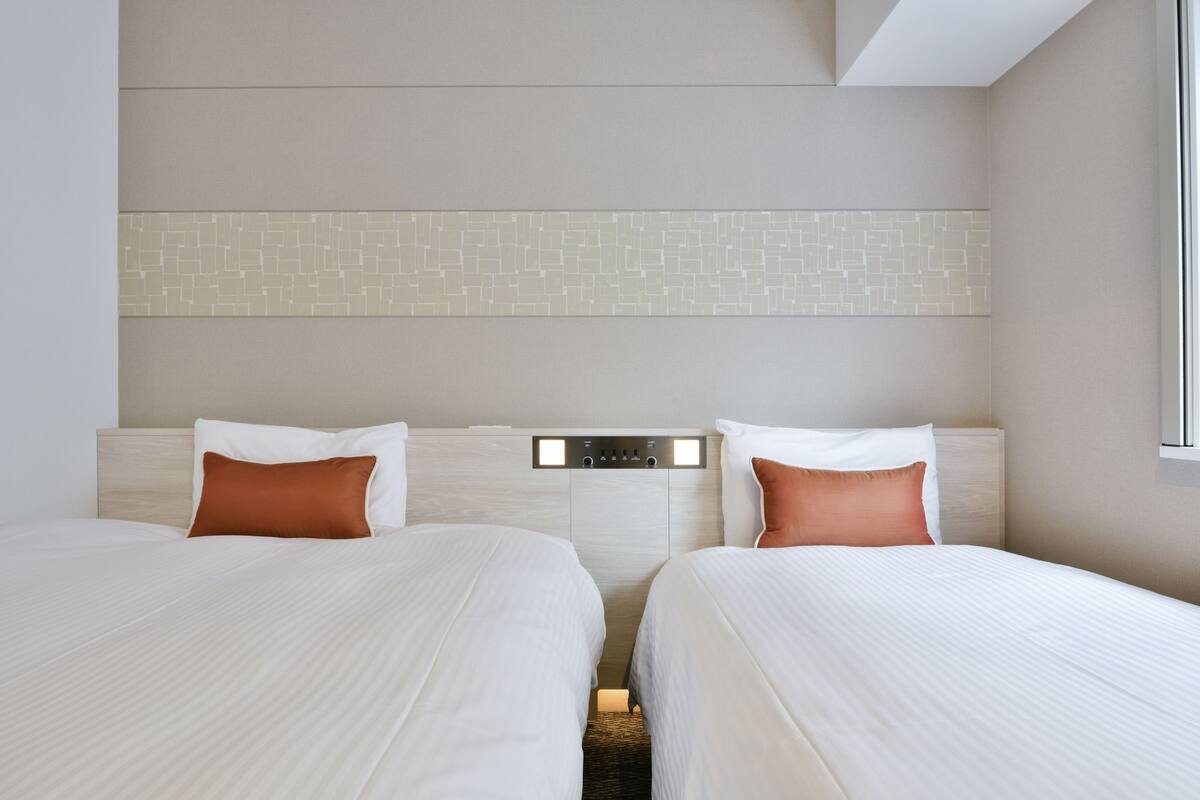 A hotel room with two beds, a control panel above the beds, and a patterned wall.