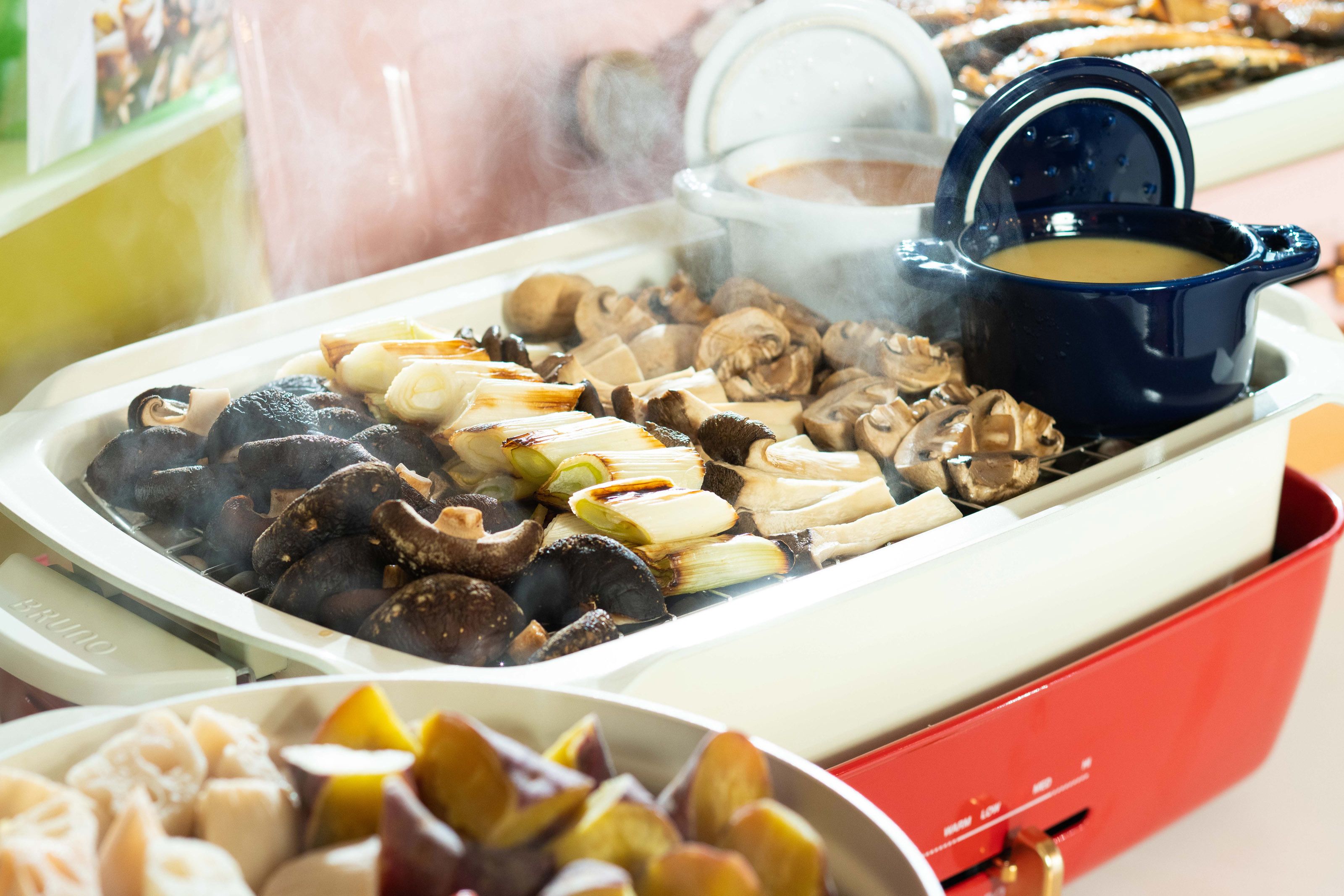 A buffet with various dishes including mushrooms, vegetables, and a pot of soup.