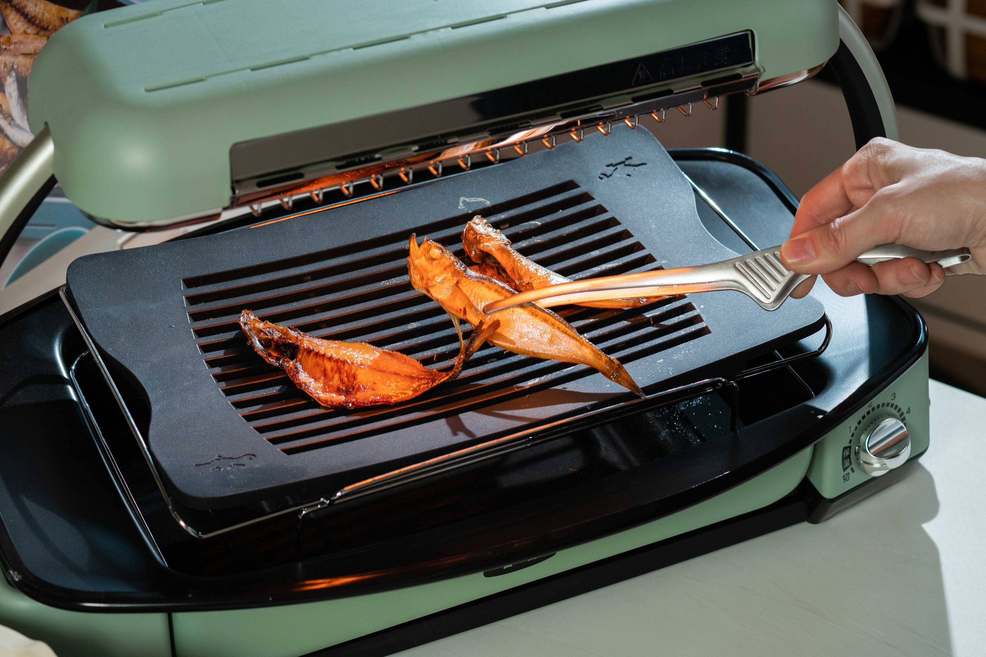 A person grilling fish on a portable outdoor grill.