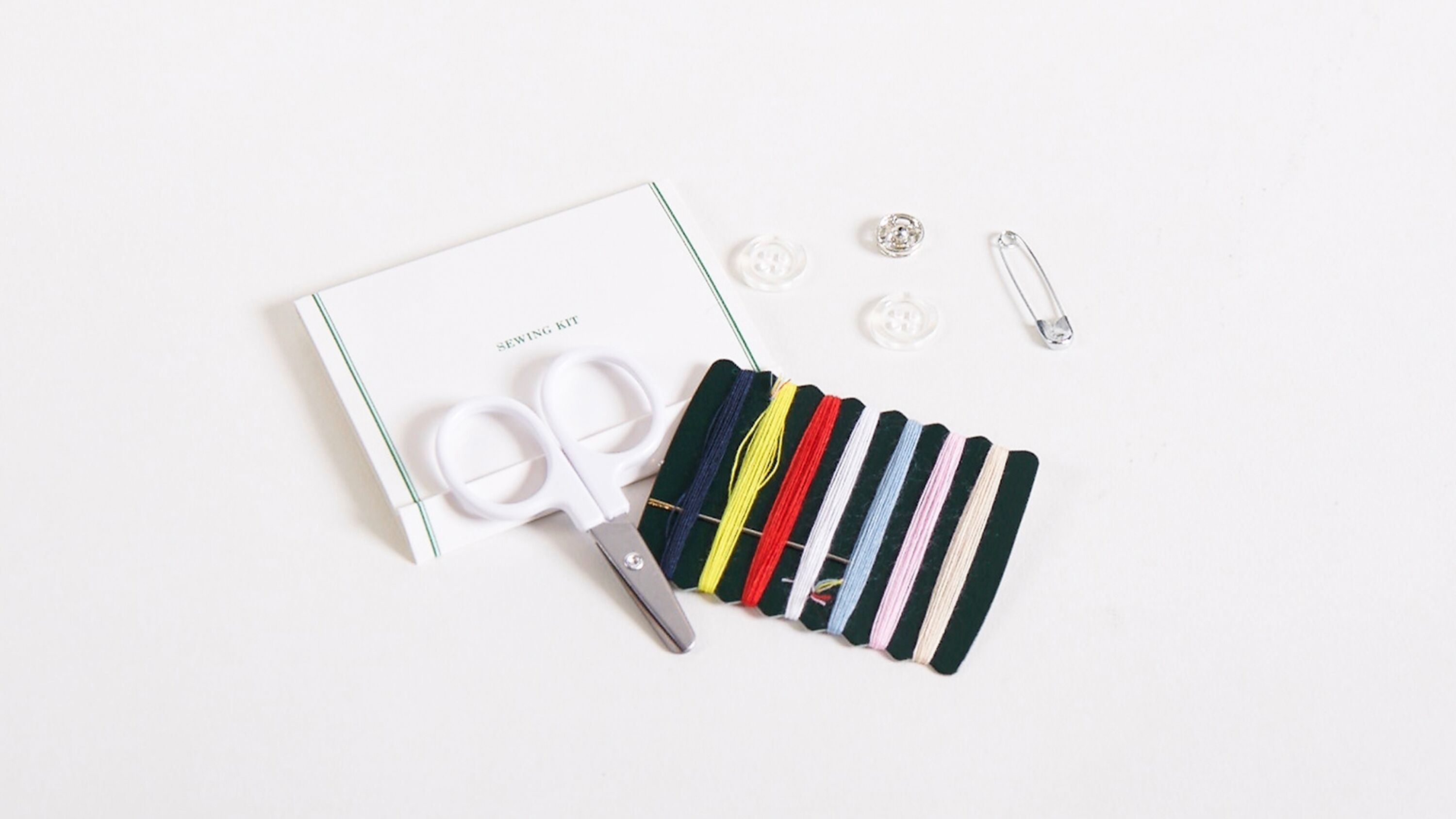 A sewing kit with scissors, thread spools, buttons, and a safety pin on a white surface.