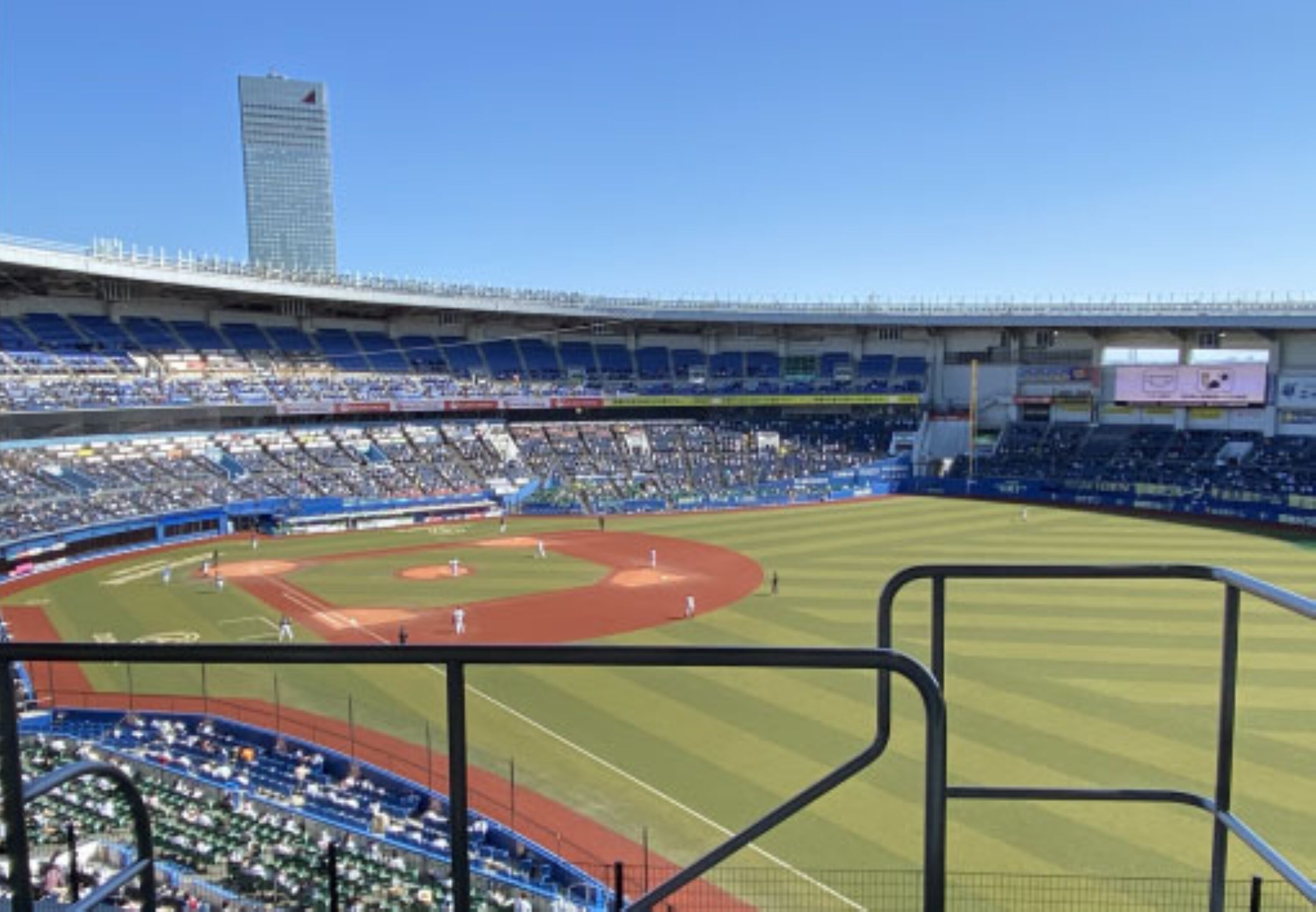 Un estadio con varios niveles de asientos, un campo de béisbol y un edificio alto al fondo.