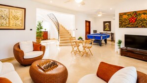 A living room with a pool table, a sofa, a coffee table with chess pieces, a TV, and a staircase leading to another level. - Luxury 6BR Villa / Pool /Walk to Beach (Punta Cana)