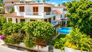 A multi-story building with a swimming pool, surrounded by lush greenery and palm trees. - Luxury 6BR Villa / Pool /Walk to Beach (Punta Cana)