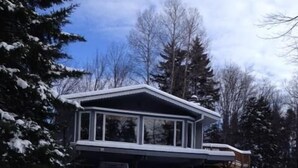 Une maison à deux étages avec un garage, entourée d’arbres couverts de neige et sous un ciel dégagé.