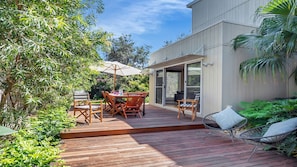 A wooden deck with a dining table and chairs, surrounded by lush greenery. - Sunshine Beach House - 25 metre walk to the beach (Culburra Beach)