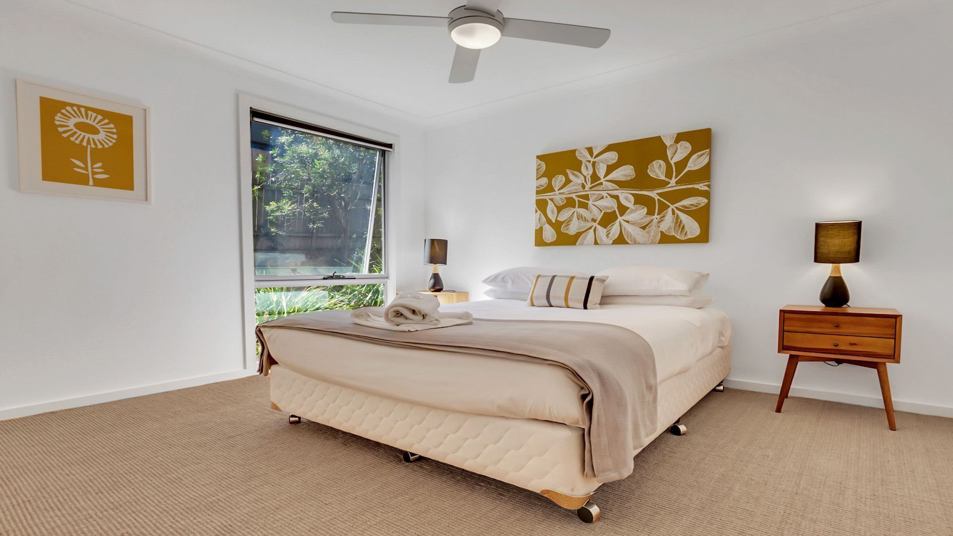 A bedroom with a bed, bedside tables, a ceiling fan, and artwork on the walls.