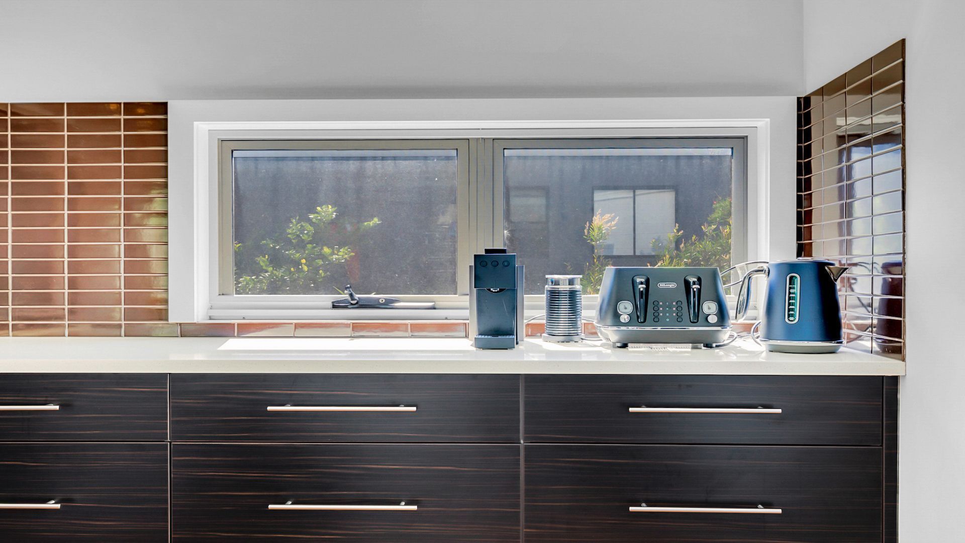 A kitchen with a window, a coffee machine, and a kettle on the counter.