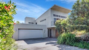 A modern two-story house with a garage, surrounded by lush greenery.