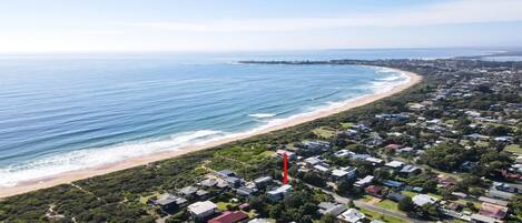 Vista aérea de una zona residencial costera con casas, una playa y un hito rojo.