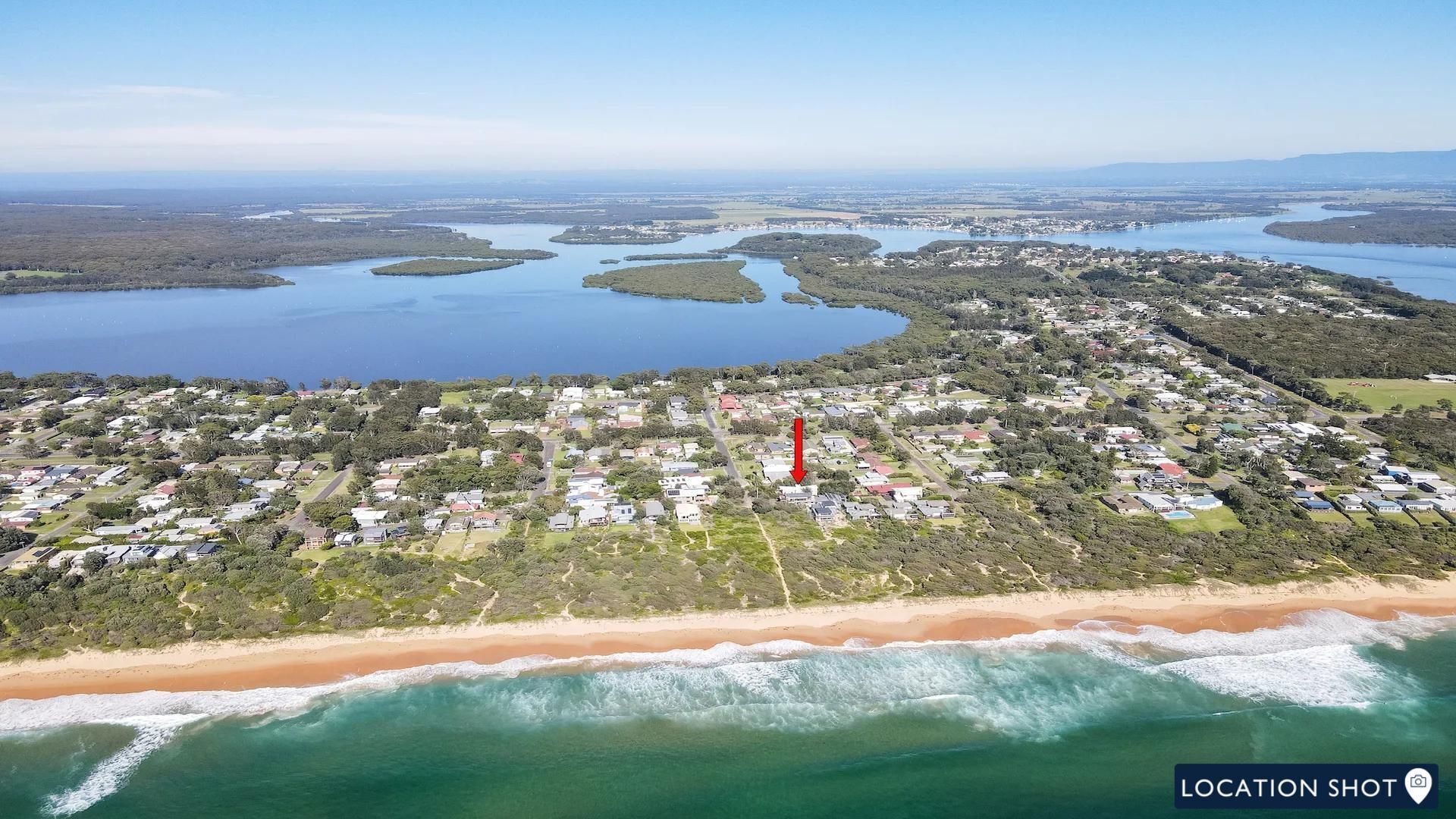An aerial view of a coastal town with a beach, residential areas, and a large body of water.