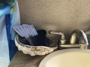 Un lavamanos con una cuenca de piedra decorativa, un grifo y un perchero con una toalla azul y un paquete de artículos de tocador.
