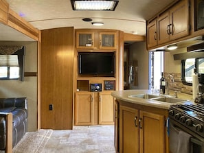 A compact RV kitchen with a built-in stove, a sink, and a television. - Poop Deck - 3 minutes from the beach and right on the Noyo harbor (Fort Bragg)