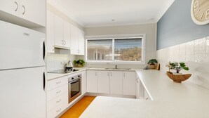 Une cuisine moderne avec des meubles blancs, un four encastré, une cuisinière et une fenêtre équipée de stores.