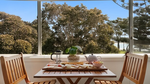 Une table en bois donnant sur des arbres et un plan d’eau, grâce à de grandes fenêtres.