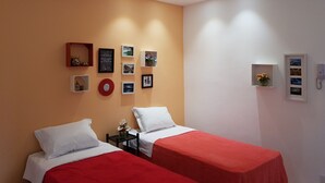 A hotel room with two beds, a small table with a vase of flowers, and a wall decorated with framed pictures and a red wreath. - Studio Lily1 - Coração do Rio (Laranjeiras)