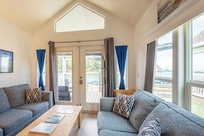 Una habitación con sofá, una mesa con libros, perchero y vista al mar a través de amplias ventanas.