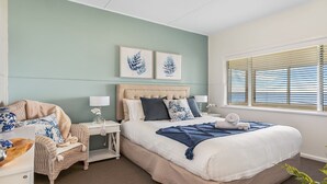 Une chambre à coucher avec un grand lit, une table de chevet, une chaise et une fenêtre avec des stores.