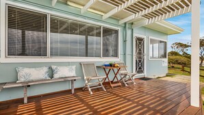 Une terrasse extérieure couverte, dotée d’un plancher en bois, d’un banc et de deux chaises.