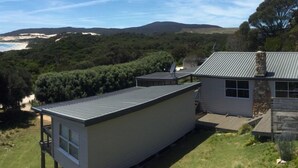 A modern house with a flat roof, a satellite dish, and a stone chimney. It is surrounded by lush greenery and overlooks a beach and hills. - Palana Beach House - sea views, pristine beach (Palana)
