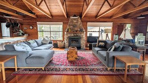 A cozy living room with two grey sofas, a stone fireplace, wooden beams, and a red patterned rug. - Palana Beach House - sea views, pristine beach (Palana)