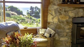 A cozy room with a stone wall, a large window overlooking a scenic landscape, a wicker basket with toiletries, and a fireplace. - Palana Beach House - sea views, pristine beach (Palana)