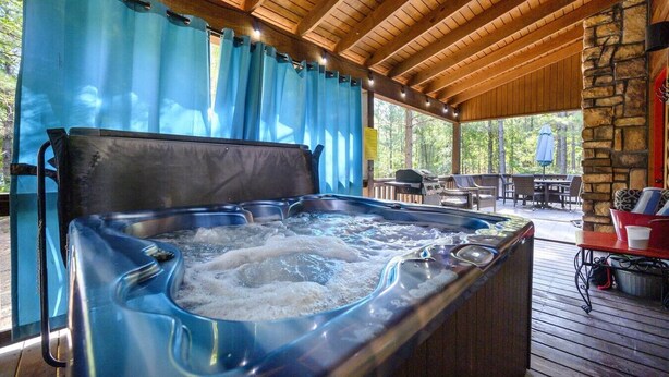 A hot tub in a covered outdoor area with wooden beams and stone walls. - Shear Pleasure|Romantic|Farmhouse Style (Hochatown)