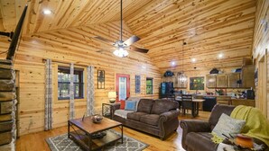 A cozy cabin interior with a wooden ceiling, a dining area, a kitchen, and a living room furnished with a sofa and a coffee table. - Shear Pleasure|Romantic|Farmhouse Style (Hochatown)