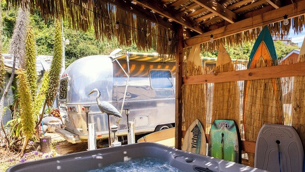 A hot tub with a wooden deck, a camper van, and surfboards against a bamboo backdrop. - Cowabunga - A luxury Airstream trailer just minutes from our private dock in the harbor and beach (Fort Bragg)