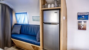 A compact RV interior with a blue sofa, a stainless steel refrigerator, and a surfboard-themed wall decoration. - Cowabunga - A luxury Airstream trailer just minutes from our private dock in the harbor and beach (Fort Bragg)