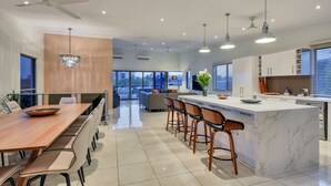 A modern kitchen with a large island, bar stools, and a dining area with a long table. - Darwin City Lights Jacuzzi (Stuart Park)