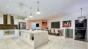 A modern kitchen with a marble island, stainless steel appliances, pendant lighting, and a dining area with a glass railing. - Darwin City Lights Jacuzzi (Stuart Park)