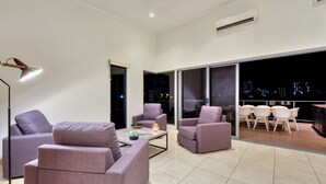 A modern living room with a sofa, armchairs, and a coffee table. There is a large window with a city view at night. - Darwin City Lights Jacuzzi (Stuart Park)