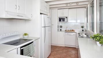 A modern kitchen with white cabinetry, a built-in oven, microwave, and dishwasher. There are potted plants on the counter and a window providing natural light.
