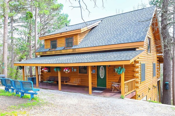 A two-story log cabin with a porch, outdoor seating, and a green door.