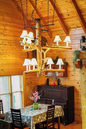 A wooden interior with a dining table, chairs, a chandelier, and a dark wooden cabinet.