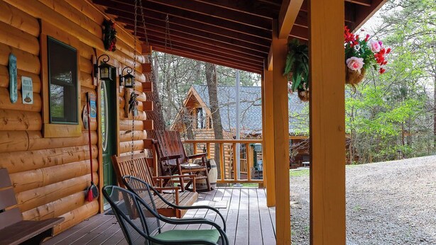 Une cabane en bois dotée d’un porche, de meubles d’extérieur et offrant une vue sur une autre cabane en arrière-plan.